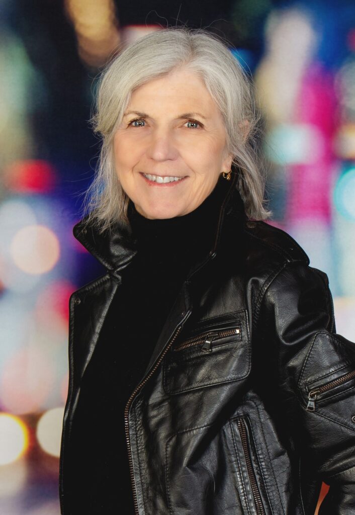 Author Marilyn F. Moriarty in a leather jacket with a blurred cityscape behind her.